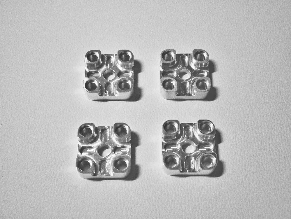 Four identical machined aluminum blocks with multiple counterbored holes