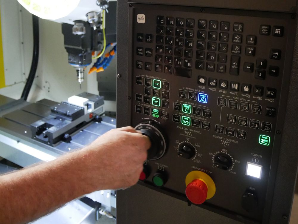 Machinist operating the FANUC control panel beside the machine vise