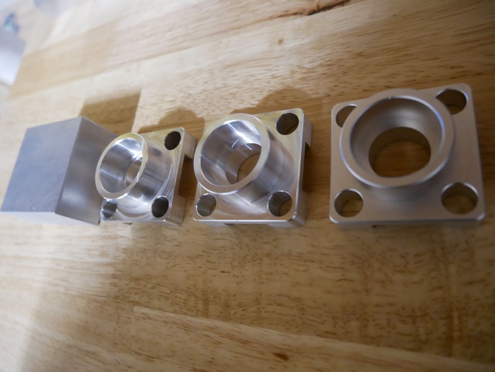 Aluminum bar stock beside three machined flanged housings at different stages