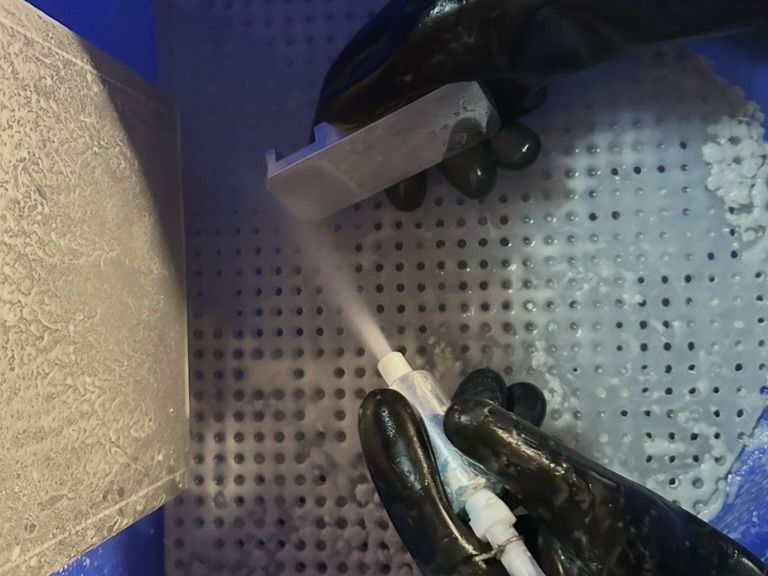 Gloved hands vapor blasting a machined part inside the blast cabinet